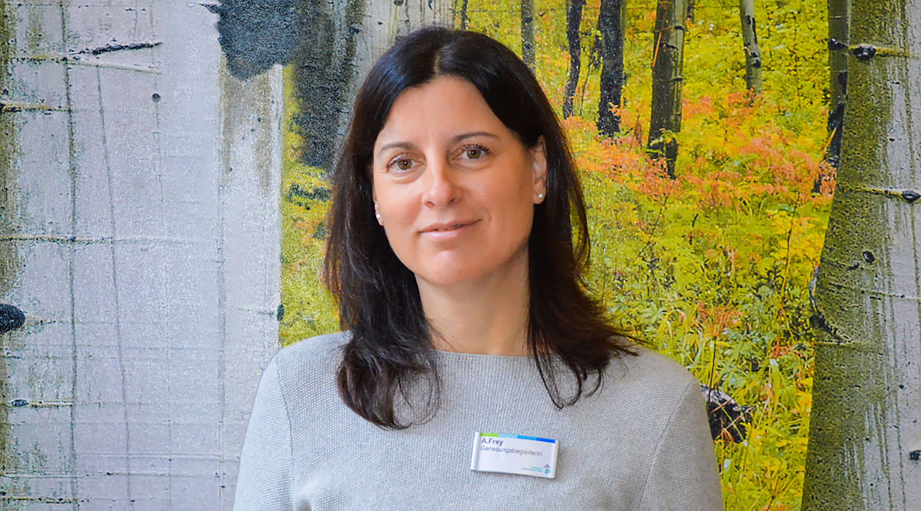 Genesungsbegleiterin Anke Frey steht vor einer Mustertapete und lächelt in die Kamera