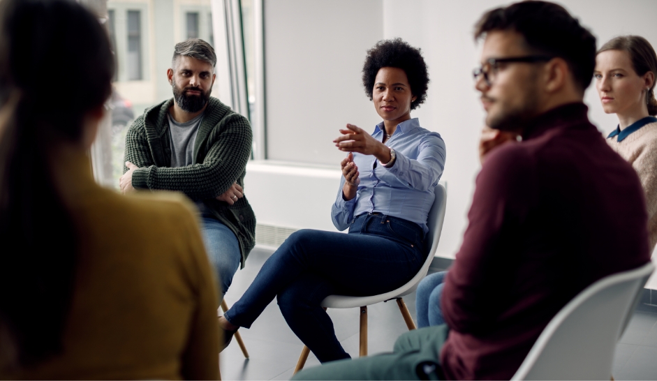 Eine Gruppe sitzt in einem Stuhlkreis mit der Therapeutin in der Mitte des Bildes