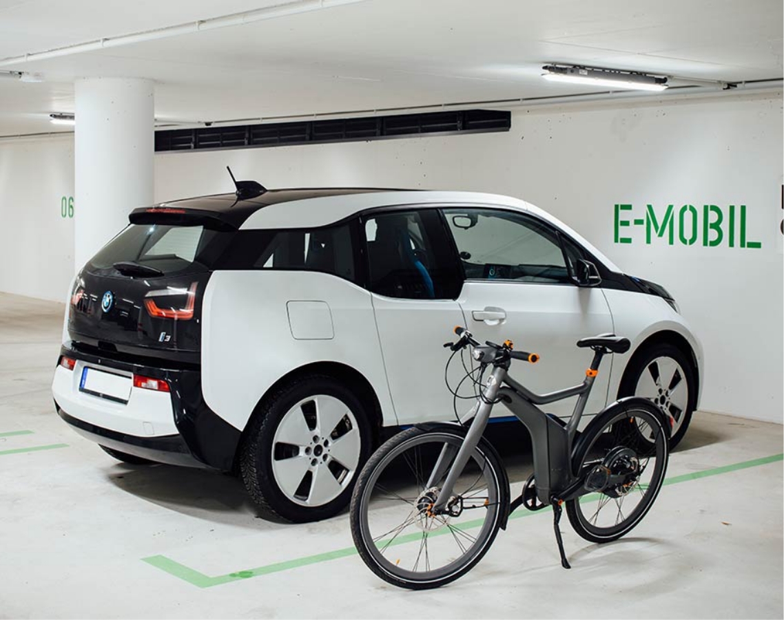 Ein E-Mobil steht auf einem speziellen Parkplatz für E-Autos und davor steht noch ein E-Bike