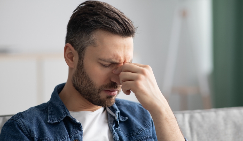 Ein Mann fasst sich zwischen den Augen an die Nase